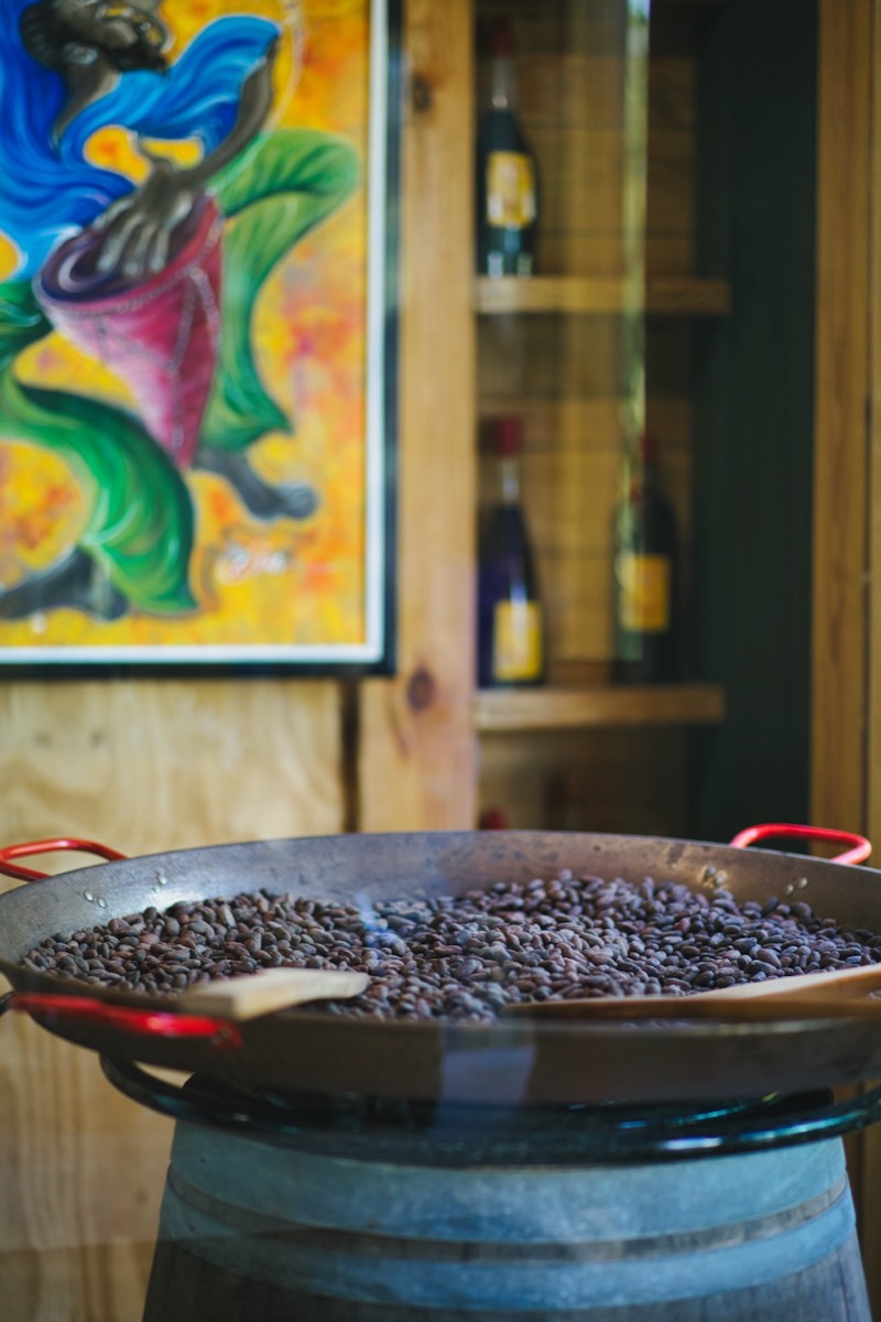 Cocoa beans roasting in a wide pan over a flame.